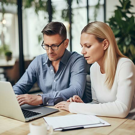 Business man and woman in business casual clothing reviewing documents on a laptop screen.